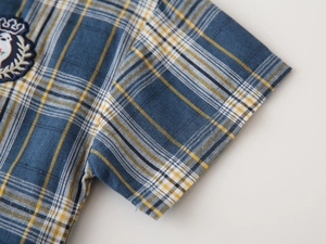 Détail d'une chemise à manches courtes à carreaux bleus et jaunes avec écusson brodé