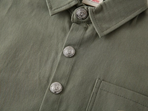 Détail de chemise garçon en coton sergé vert armée avec boutons étoile et poche poitrine