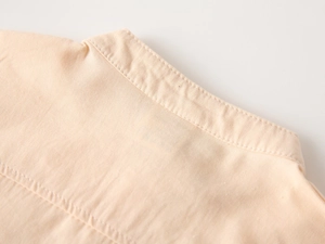 Détail de la texture en coton orange clair et des coutures du col en V sur chemise garçon