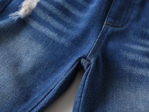 Detail of boys distressed denim jeans featuring ripped fabric and whisker wash effects