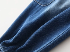 Detailed macro view of medium blue washed denim fabric with pocket stitching and elastic cuff