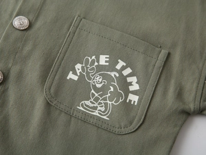 Détail d'une chemise olive pour garçons avec poche poitrine et motif de dessin animé
