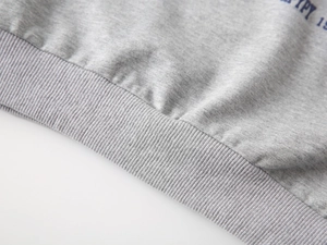 Détail du sweat-shirt en tricot gris montrant les poignets côtelés et l'imprimé bleu