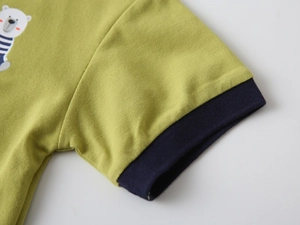 Détail d'un polo vert pour enfant avec bord-côte bleu marine et imprimé ours mignon