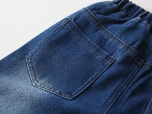 Detailed close-up of blue denim kids jeans back pocket with elastic waist and washed texture