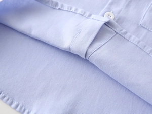 Close-up of light blue cotton shirt fabric featuring white button and neat stitching details