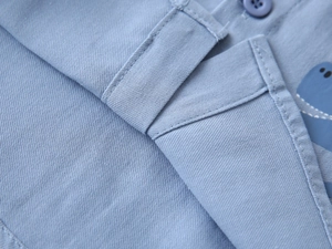 Détail de chemise bleue pour garçon montrant couture précise, bouton et motif dinosaure