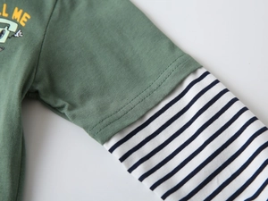 Dettaglio ravvicinato delle maniche a righe blu e tessuto verde con stampa CALL ME