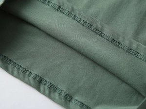 Dettaglio dell'orlo cucito e del morbido tessuto di cotone verde sulla maglia da bambino