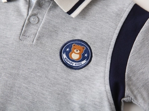 Close-up of boys grey knit polo shirt featuring bear embroidery and navy trim