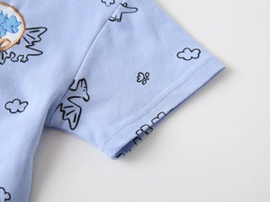 Detail of light blue polo shirt featuring cartoon dinosaur prints and embroidered badge