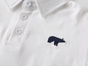 Macro detail of white cotton polo shirt featuring premium navy blue bear embroidery and buttons