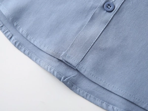Detail of light blue cotton shirt featuring a curved hem and matching four-hole buttons