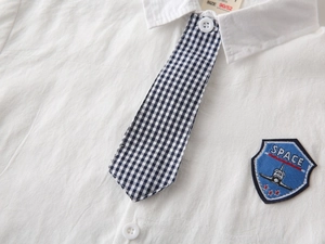Close-up of white cotton shirt featuring space shuttle embroidery and grid pattern necktie