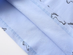 Close-up of baby polo shirt stitching and soft light blue cotton fabric with dinosaur print