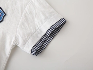 Close-up of white cotton shirt sleeve with blue gingham trim and embroidered patch detail