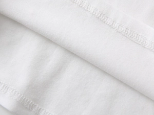 Close-up of white knitted cotton fabric showing high-quality overlock stitching and hem detail
