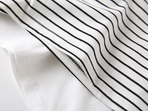 Detail shot of boys' polo shirt featuring black and white stripes and white layered hem