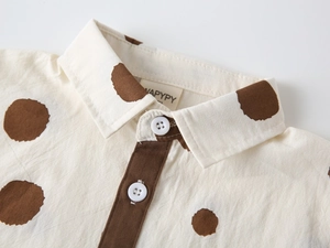 Detail of child's cream shirt featuring brown polka dots and classic button collar