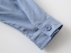 Close-up of light blue cotton shirt cuff with single button and detailed stitching