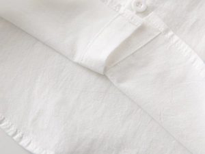 Close-up of white cotton fabric texture and button detail on children short sleeve shirt