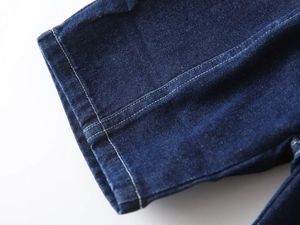 Détail du tissu denim bleu foncé montrant les surpiqûres blanches et la texture sergé