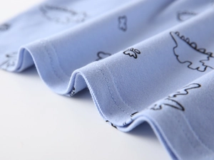 Detailed close-up of light blue cotton knit fabric with black dinosaur prints and fine stitching