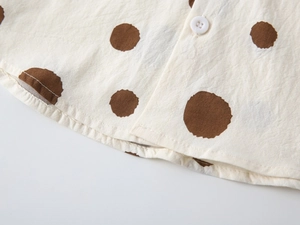 Close-up of beige linen shirt fabric with large brown polka dots and a white button