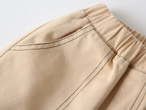 Detail of light beige cotton pants featuring elastic waist and dark contrast stitching