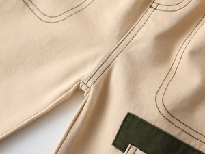 Close-up of beige cotton twill pants featuring contrast stitching and green patchwork detail
