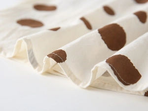 Detailed macro view of cream cotton fabric with large brown polka dots and natural texture