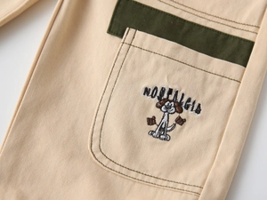 Detail of embroidered dog on kids beige cotton trousers with green patchwork pocket
