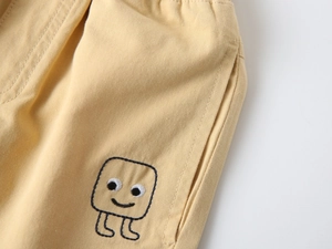 Detail of yellow cotton shorts featuring playful black monster embroidery on the side pocket