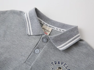 Détail du col d'un polo en coton gris avec rayures blanches et broderie sur la poitrine