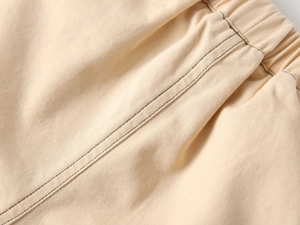Detail of light beige twill cotton pants showing elastic waistband and double stitching