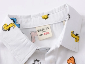 Close-up of the collar and brand label on a white cotton shirt with cartoon dinosaur prints