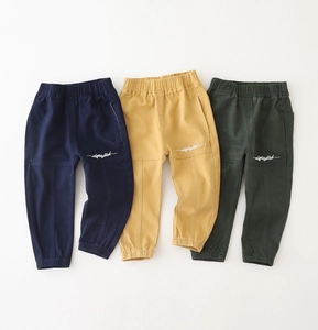 Flat lay of three boys' cotton cargo pants in navy, yellow, and green with embroidery