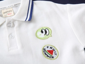 Détail d'un polo blanc en coton pour garçon avec broderie de fruits et col rayé