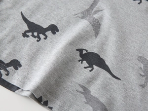 Close-up of grey knitted fabric with black dinosaur silhouette prints for a kids polo shirt
