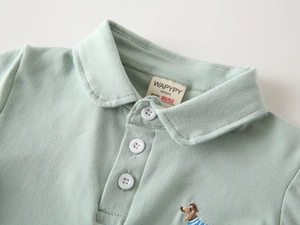 Dettaglio macro della polo in cotone verde menta con bottoni bianchi e ricamo a cane