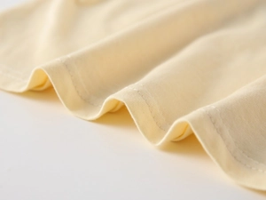 Macro shot of cream cotton knit fabric with durable double-needle stitching on the edges