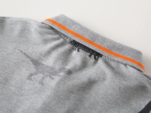 Detail of grey kids polo shirt collar with orange stripes and dinosaur print