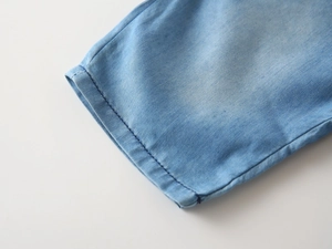 Detailed macro view of light blue denim fabric with reinforced hem stitching and soft texture