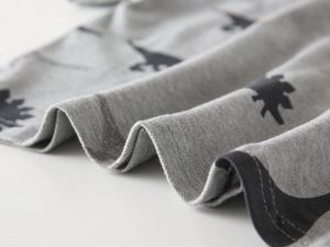 Detailed view of grey polo shirt fabric with black dinosaur prints and hem stitching