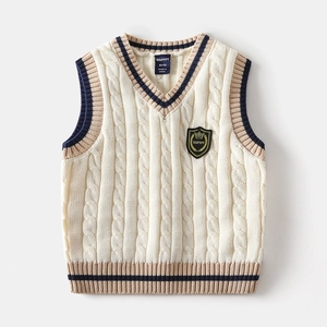 Macro detail of V-neck cable knit kids vest with navy stripes and a crown shield badge