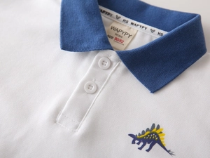 Close-up of boys white cotton polo shirt collar with navy trim and stegosaurus embroidery