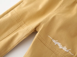 Detail of boys' cargo pants showing yellow twill fabric and white script embroidery