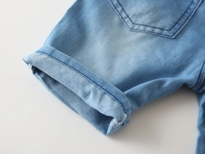 Close-up of light blue denim shorts featuring rolled cuffs and stitched back pocket details