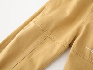 Detail of yellow cotton cargo pants showing double stitching and white letter embroidery