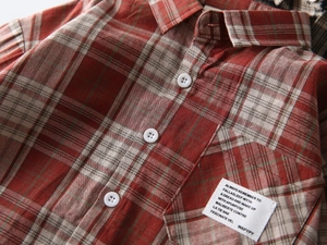 Detailed close-up of red and beige checkered cotton shirt with white button and woven pocket label